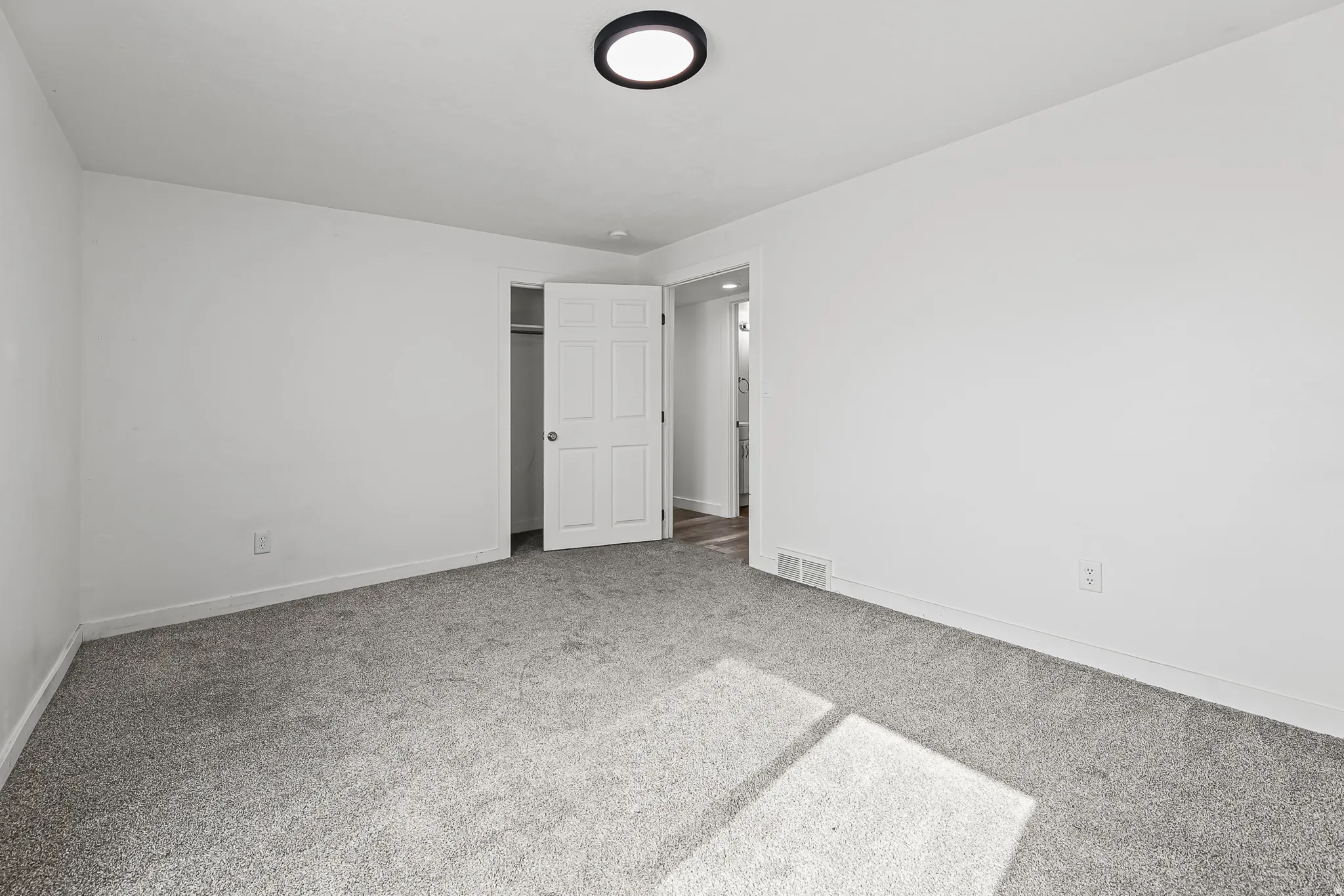 Spacious interior room with light gray carpet, white painted walls, and a contemporary flush-mount ceiling light