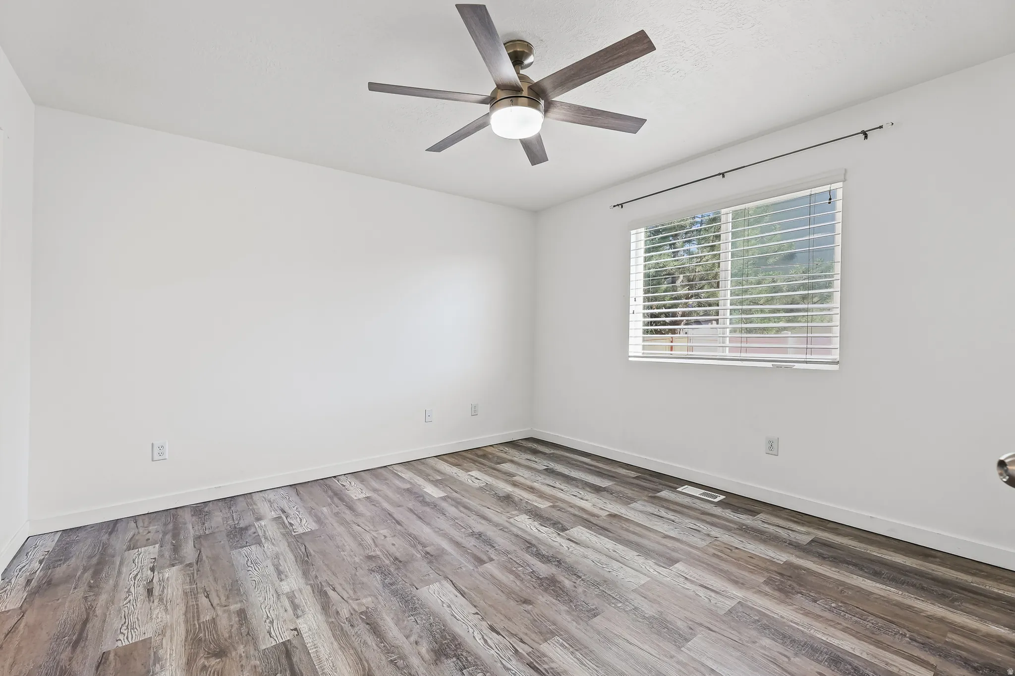 Room featuring wood-finish flooring, a window with blinds, a ceiling fan with light fixture, white walls, and white baseboards