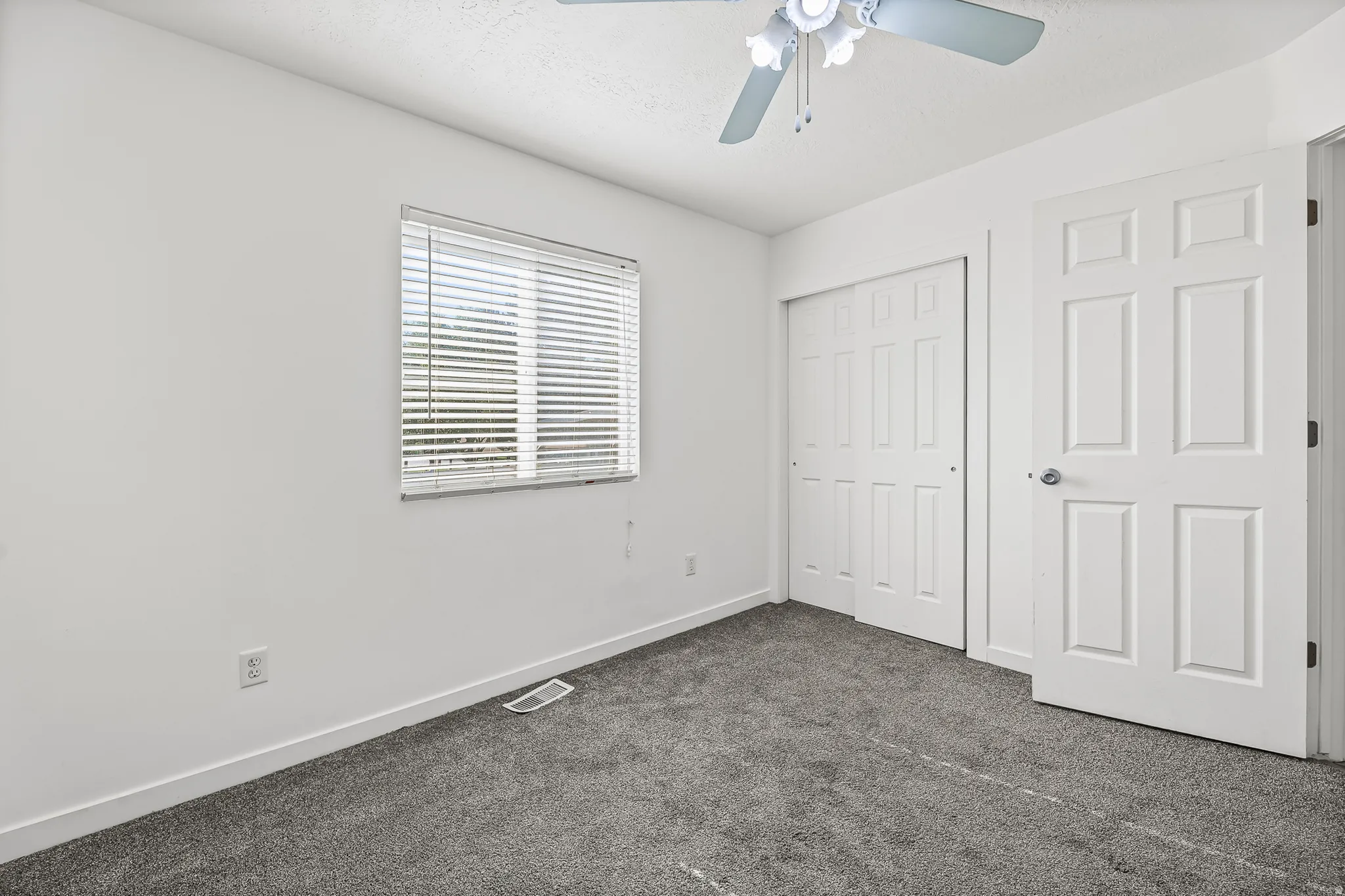 Bright room featuring gray carpet flooring, white walls, and a ceiling fan with light fixture