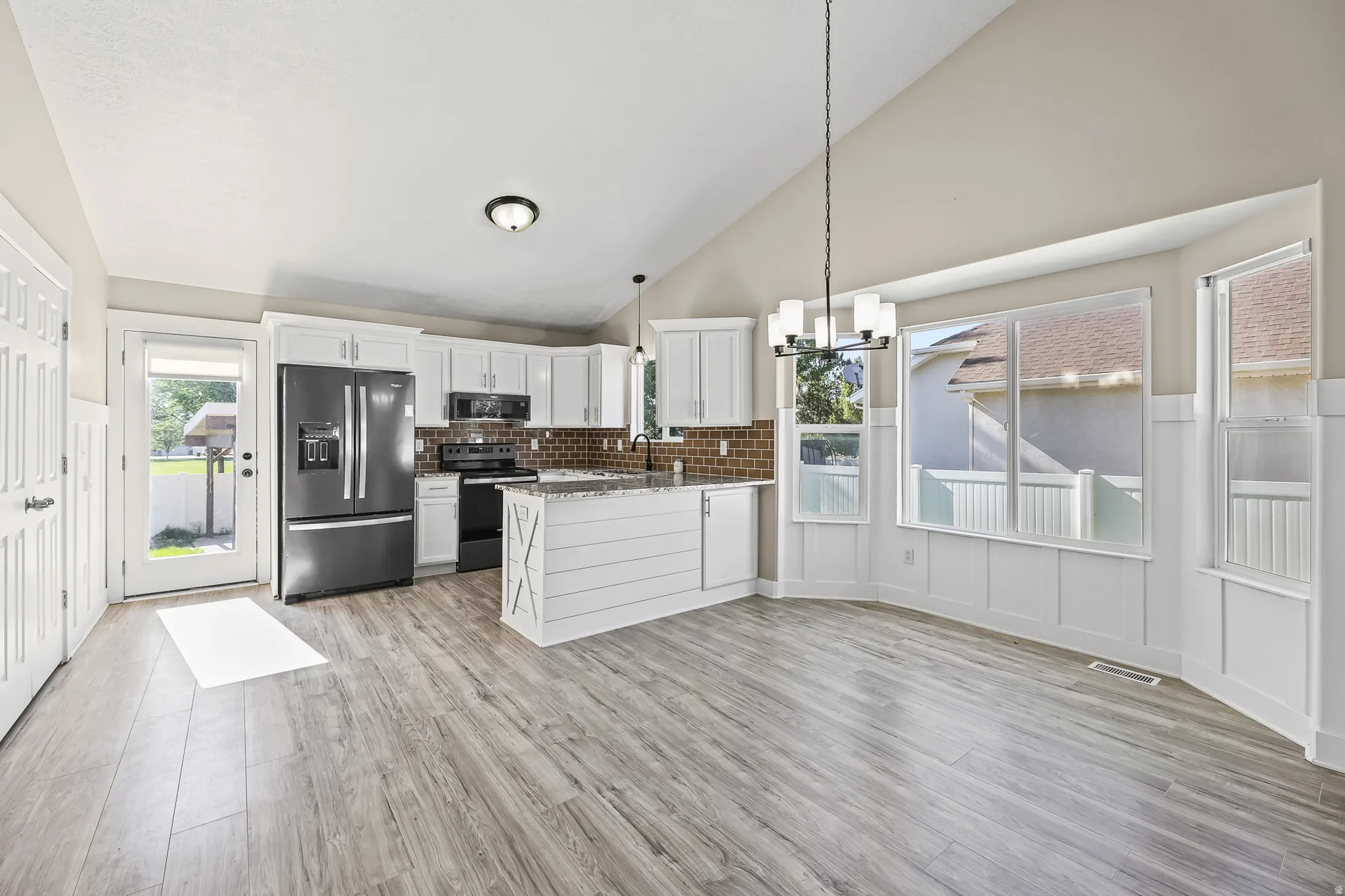 Open-concept kitchen and dining area featuring vaulted ceilings, wood-finish flooring, white cabinetry, and a granite-topped island with shiplap detail