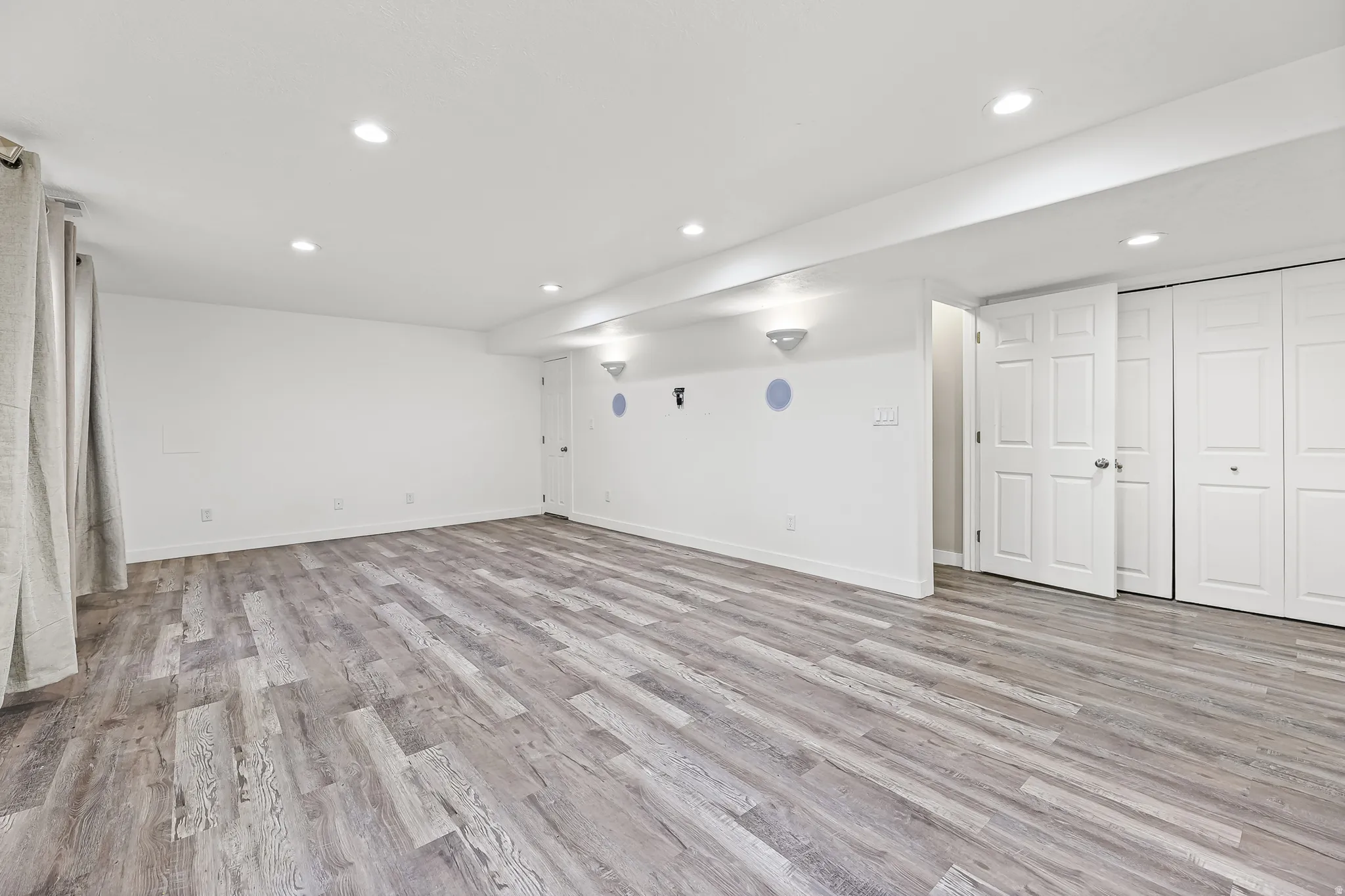 Spacious room featuring wood-finish flooring, recessed lighting, white walls, and bi-fold closet doors