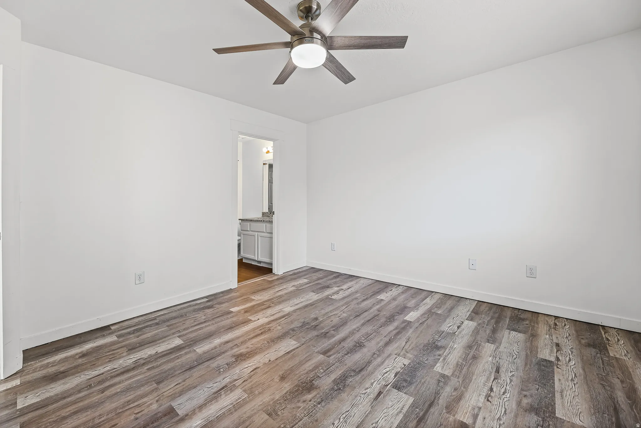 Spacious room featuring wood-finish flooring, white walls, and a ceiling fan with integrated lighting