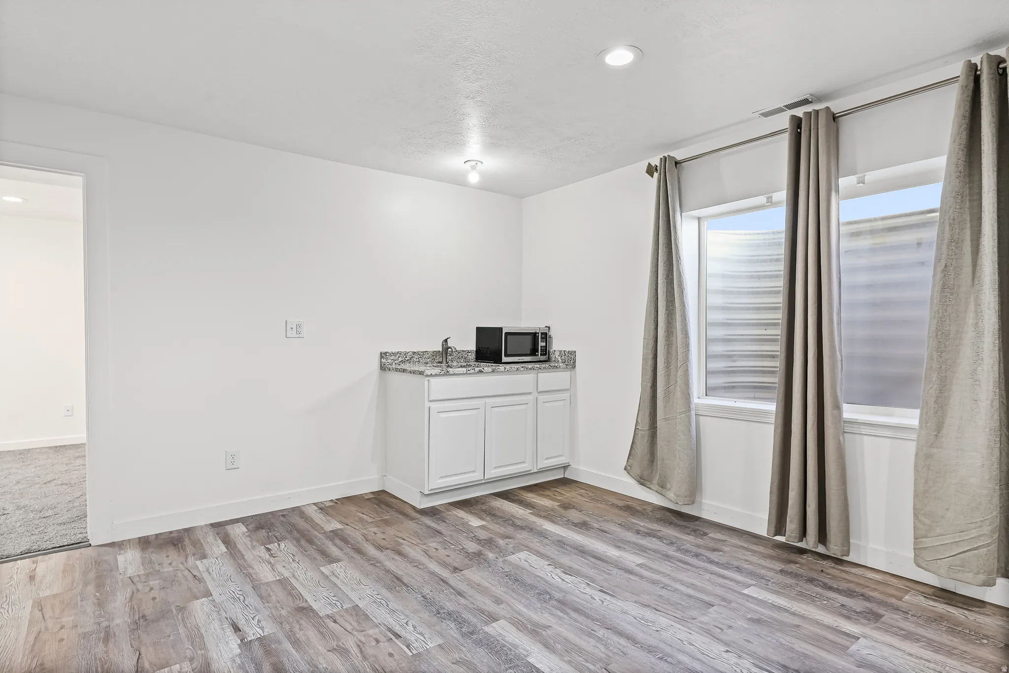 Spacious room featuring wood-finish flooring, white baseboards, and bright recessed lighting