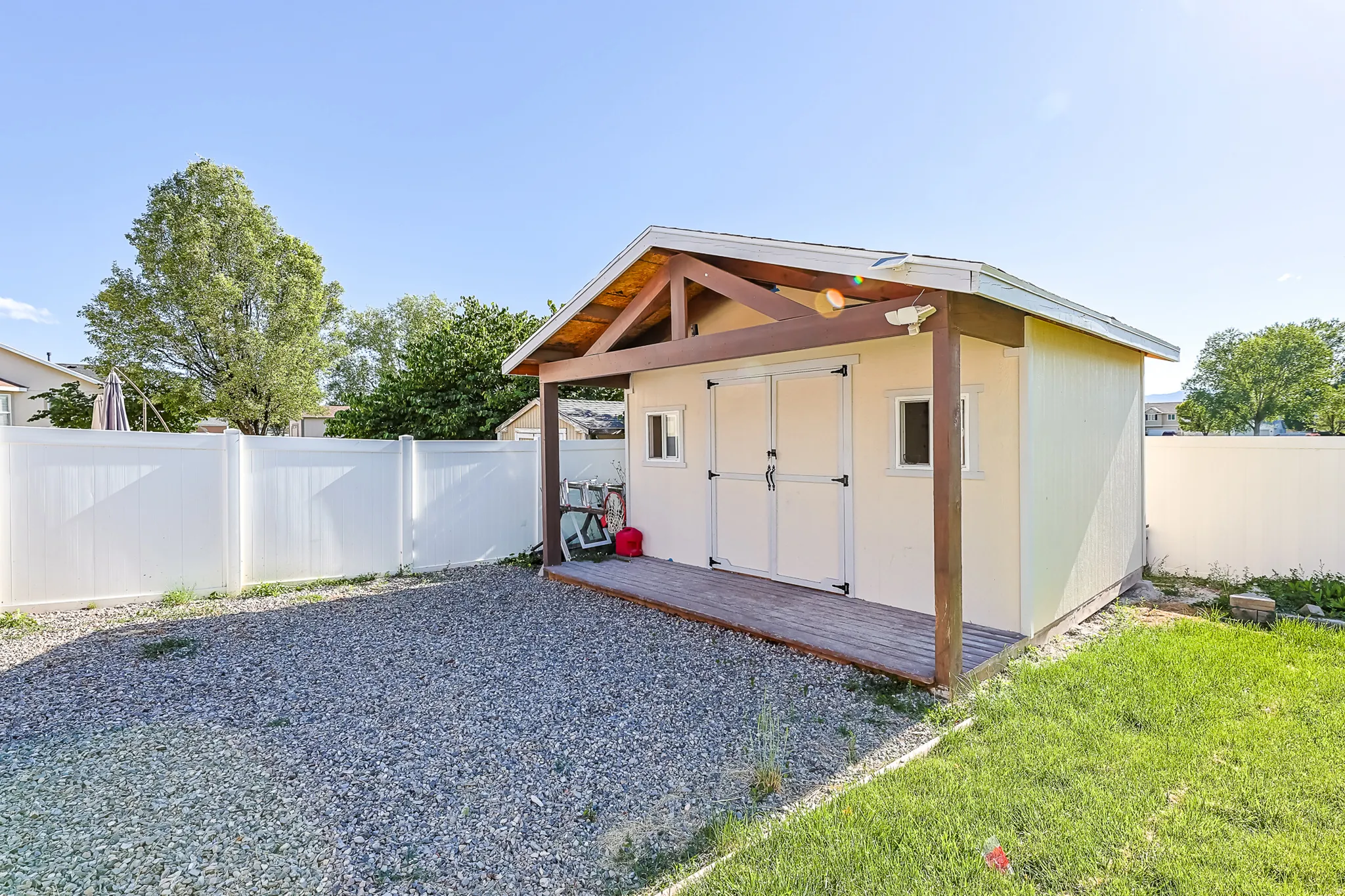 Detached shed featuring a covered wood-finish deck, double entry doors, two windows, and a vinyl fence