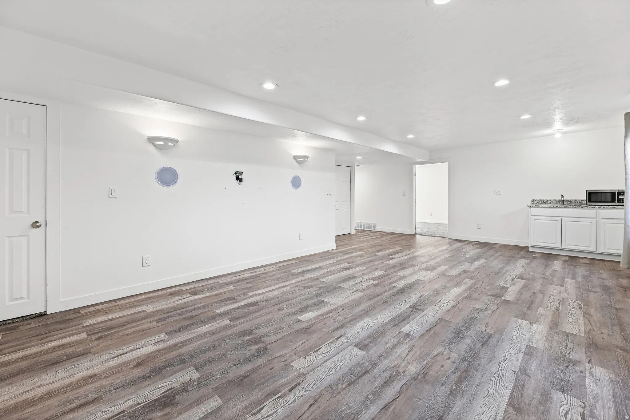 Expansive open-concept room featuring wood-finish flooring, recessed lighting, and a built-in wet bar with a stone countertop and white cabinetry
