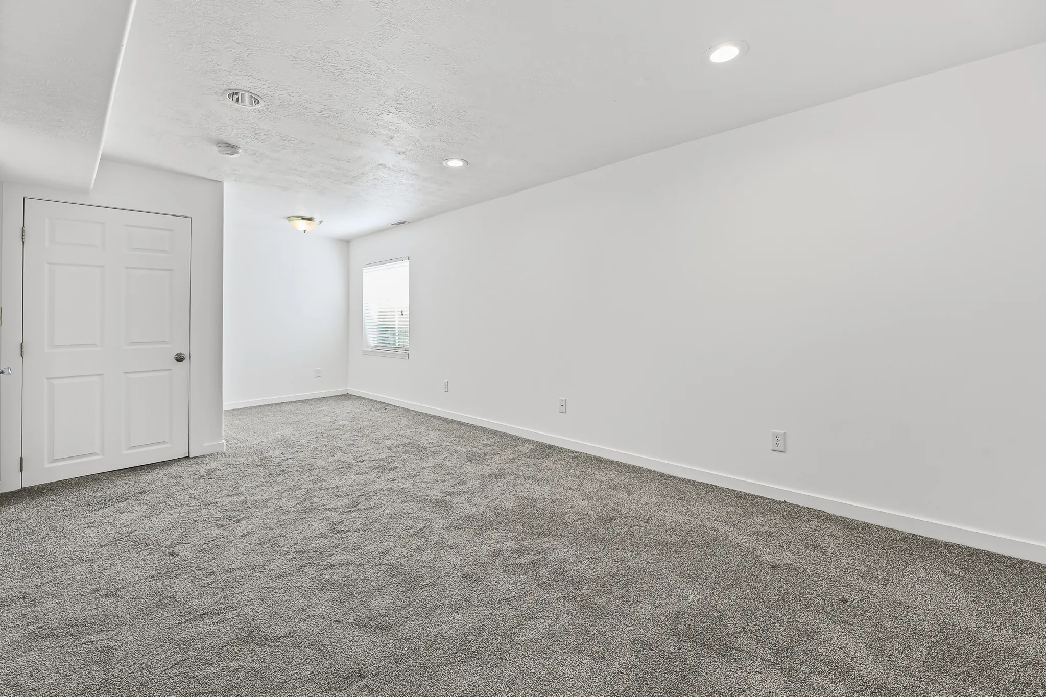 Spacious interior room featuring gray carpeting, white walls, recessed ceiling lights, and an overhead light fixture