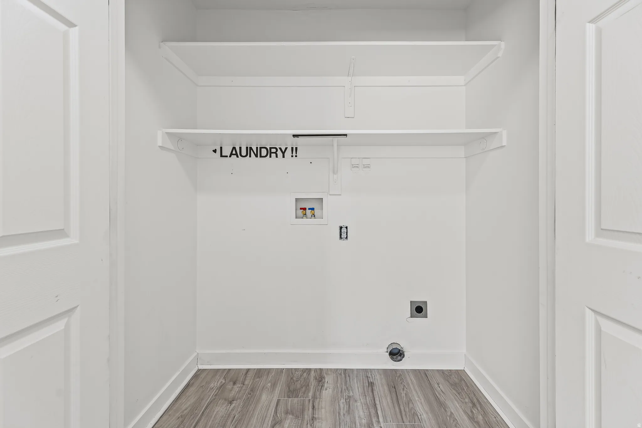 Dedicated laundry area featuring white walls, wood-finish flooring, and two integrated shelves