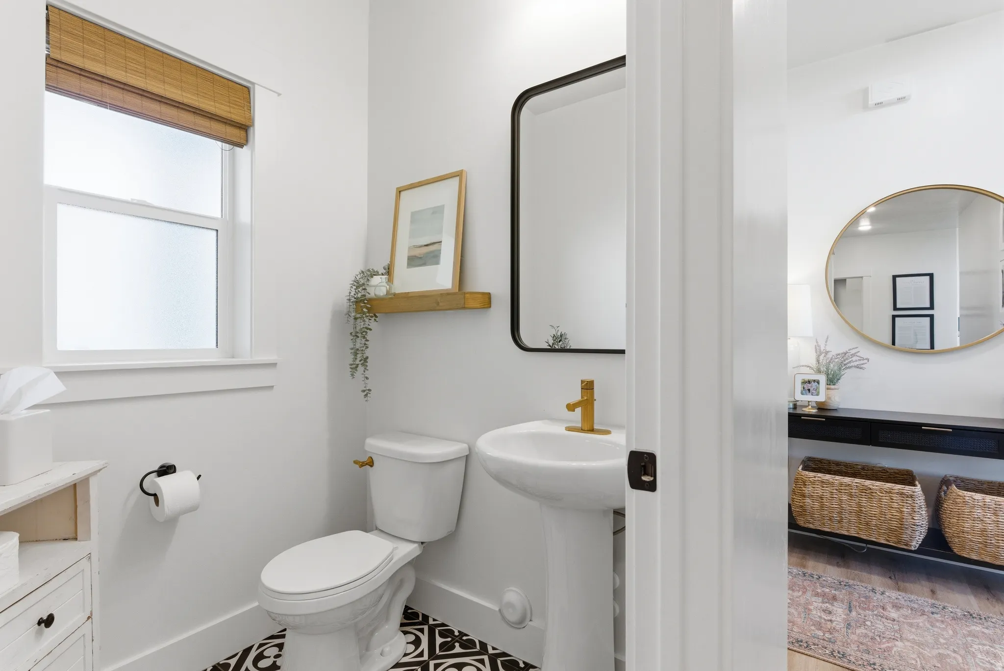 Pedestal sink with gold-finish faucet, black-frame mirror, and patterned floor tile