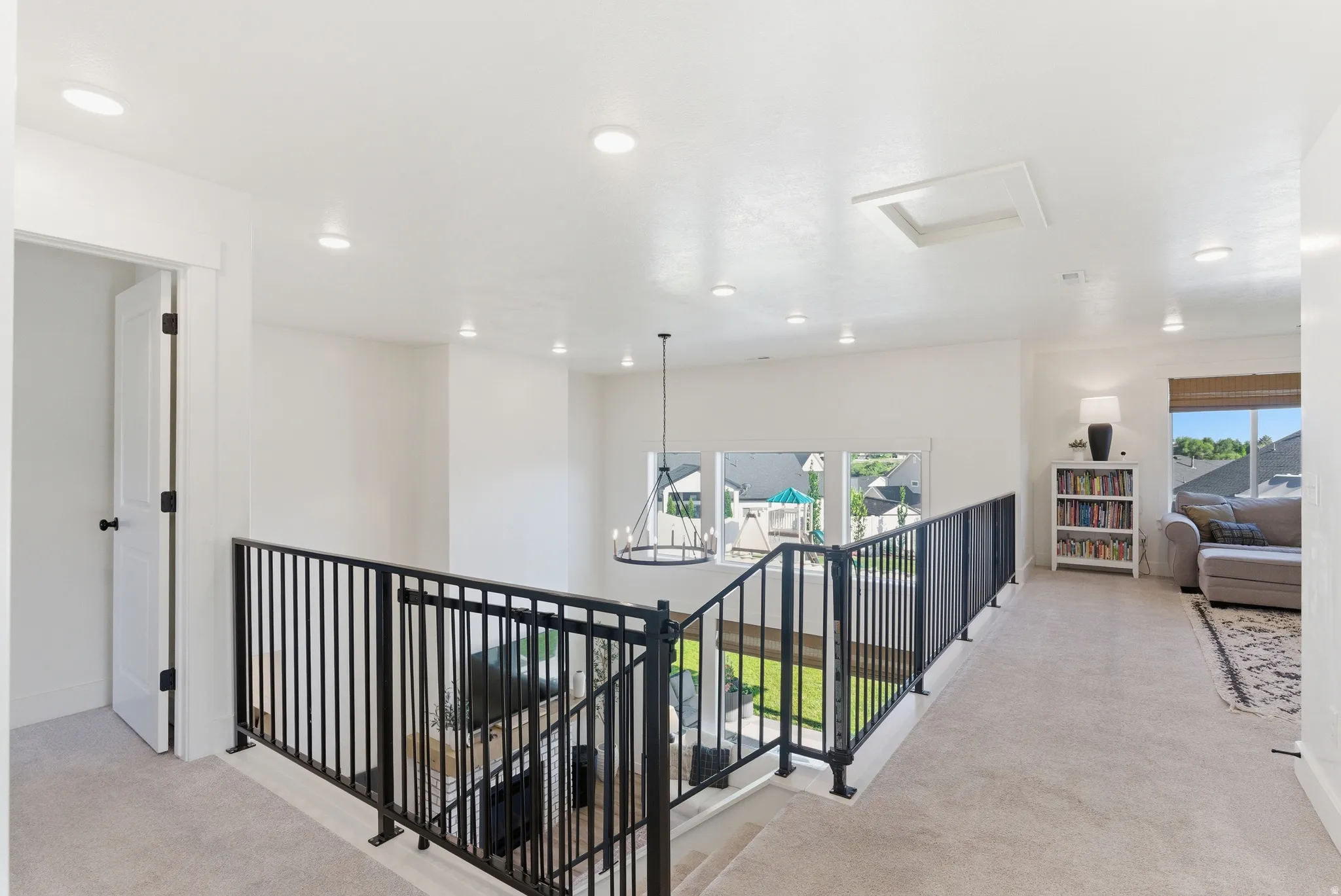 Upper-level landing featuring light-colored carpeting, recessed ceiling lights, and a black wrought iron railing overlooking a lower space