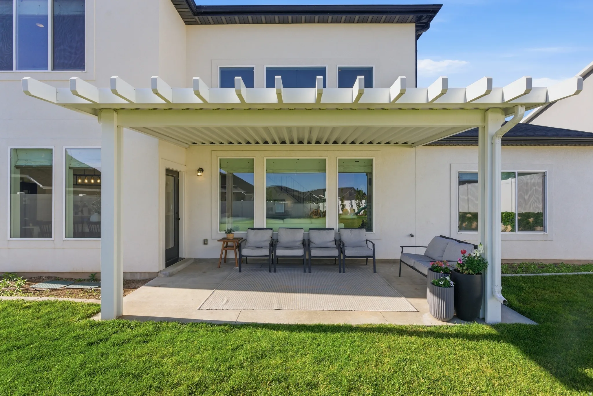 Rear patio with a white pergola, concrete flooring, and an exterior door