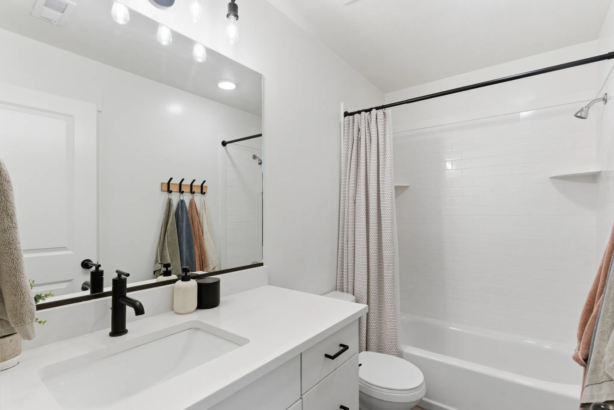 Bathroom featuring a built-in vanity with an integrated sink and matte black faucet, a large wall mirror with overhead lighting, and a bathtub with subway tile surround