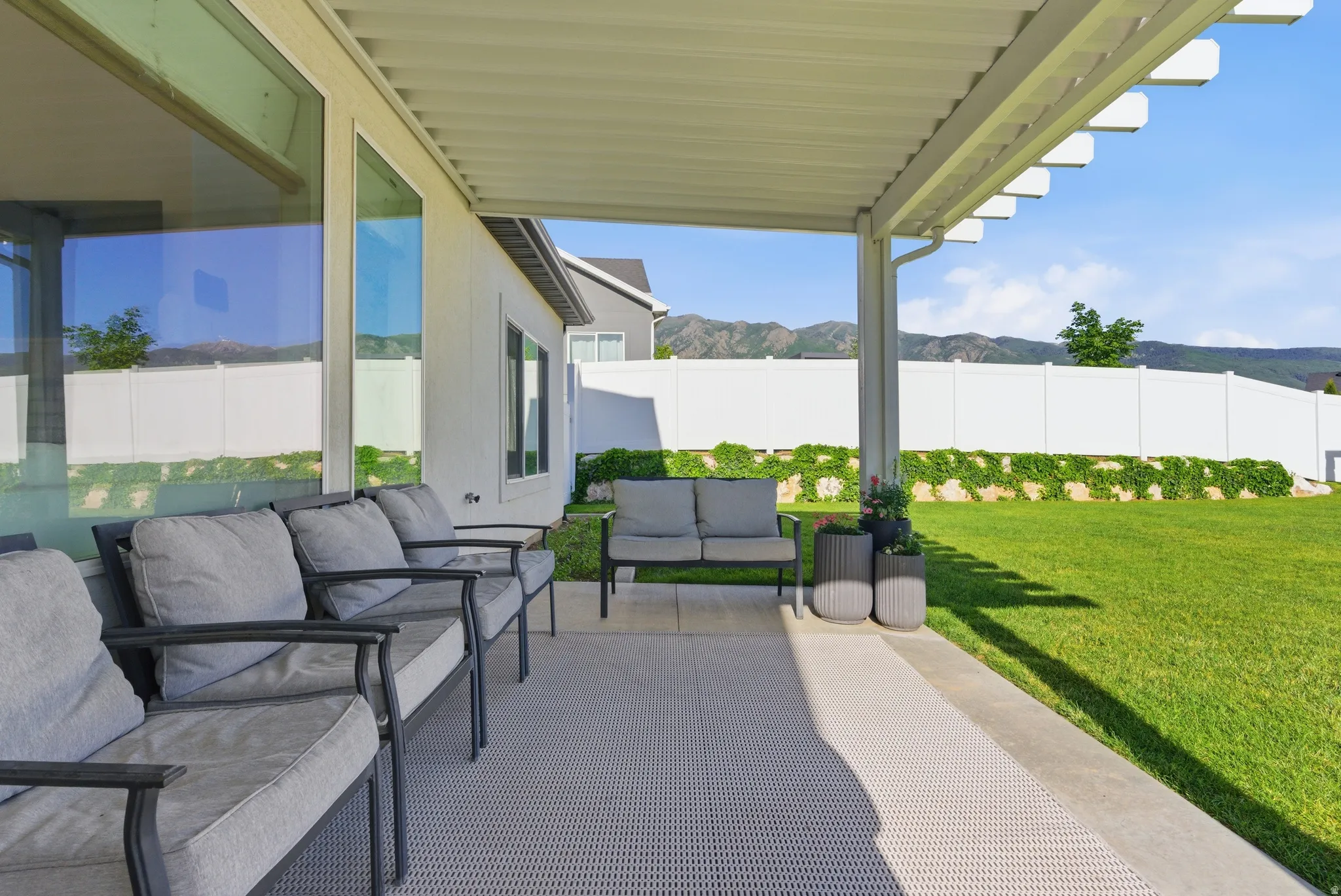 Expansive covered patio featuring a solid roof structure with open pergola details, a concrete slab base, and direct access to a large, well-maintained lawn
