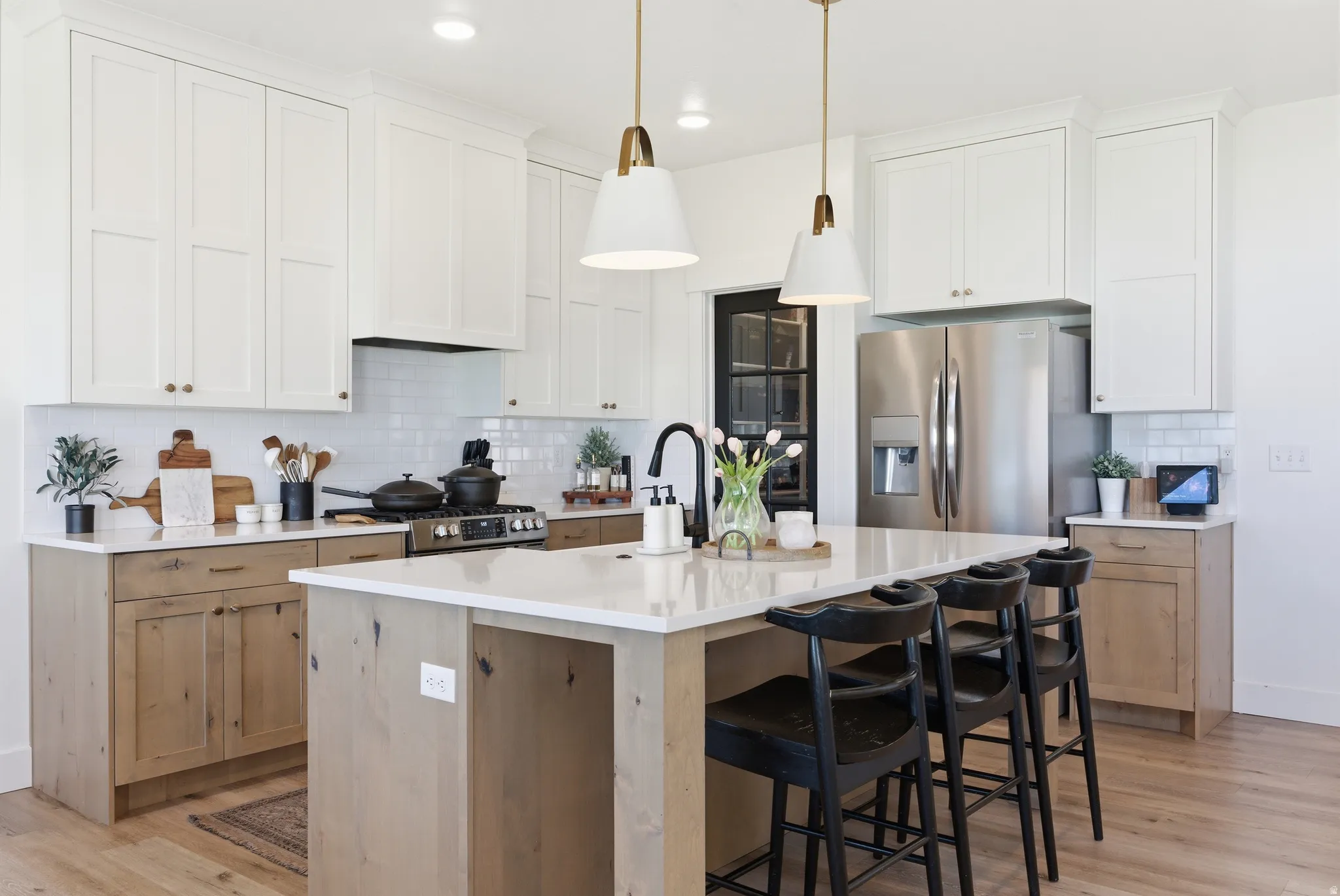 Modern kitchen featuring a central island with countertop seating, two-tone cabinetry with white upper and wood-finish lower cabinets, stainless steel appliances, a subway tile backsplash, and recessed lighting with pendant fixtures