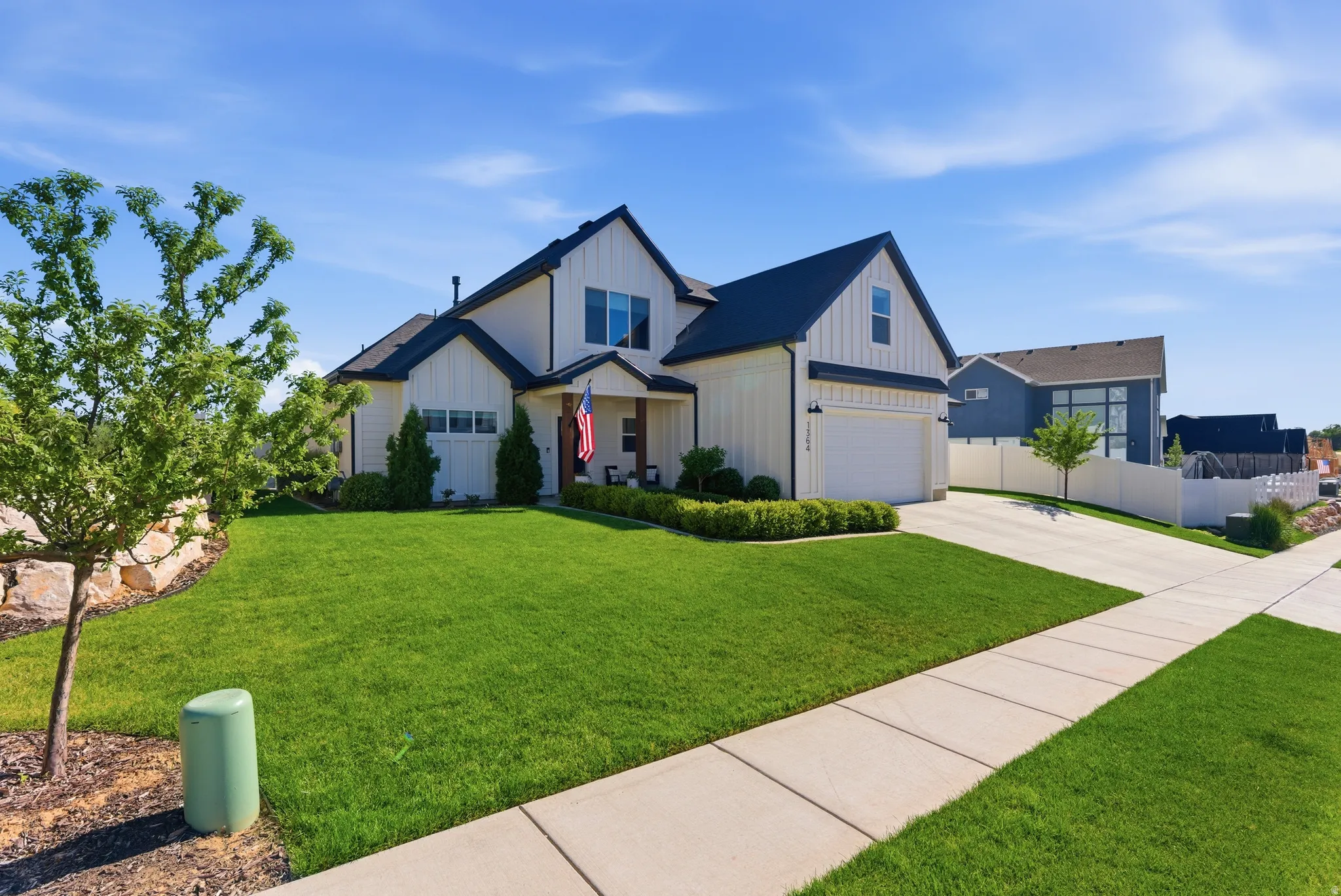 Contemporary farmhouse-style residence featuring white board and batten siding with dark trim, a black gabled roof, an attached two-car garage, and a concrete driveway