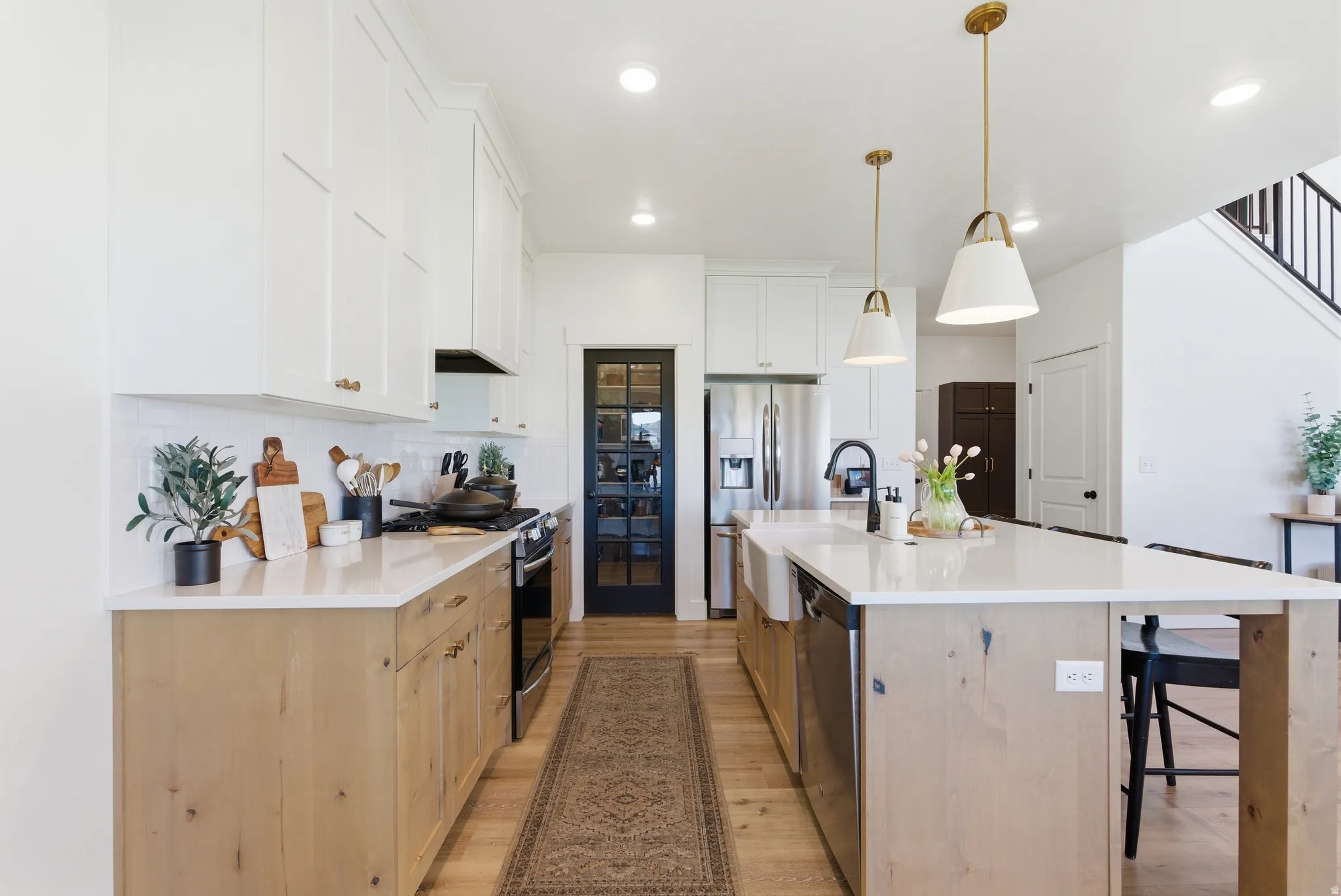 Modern kitchen featuring an extended island with a farmhouse sink, stainless steel appliances, and wood-finish flooring