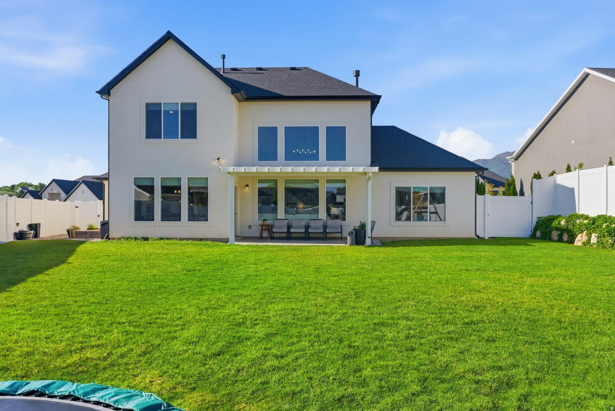 Expansive backyard featuring a lush green lawn, full privacy fencing, and a covered patio area