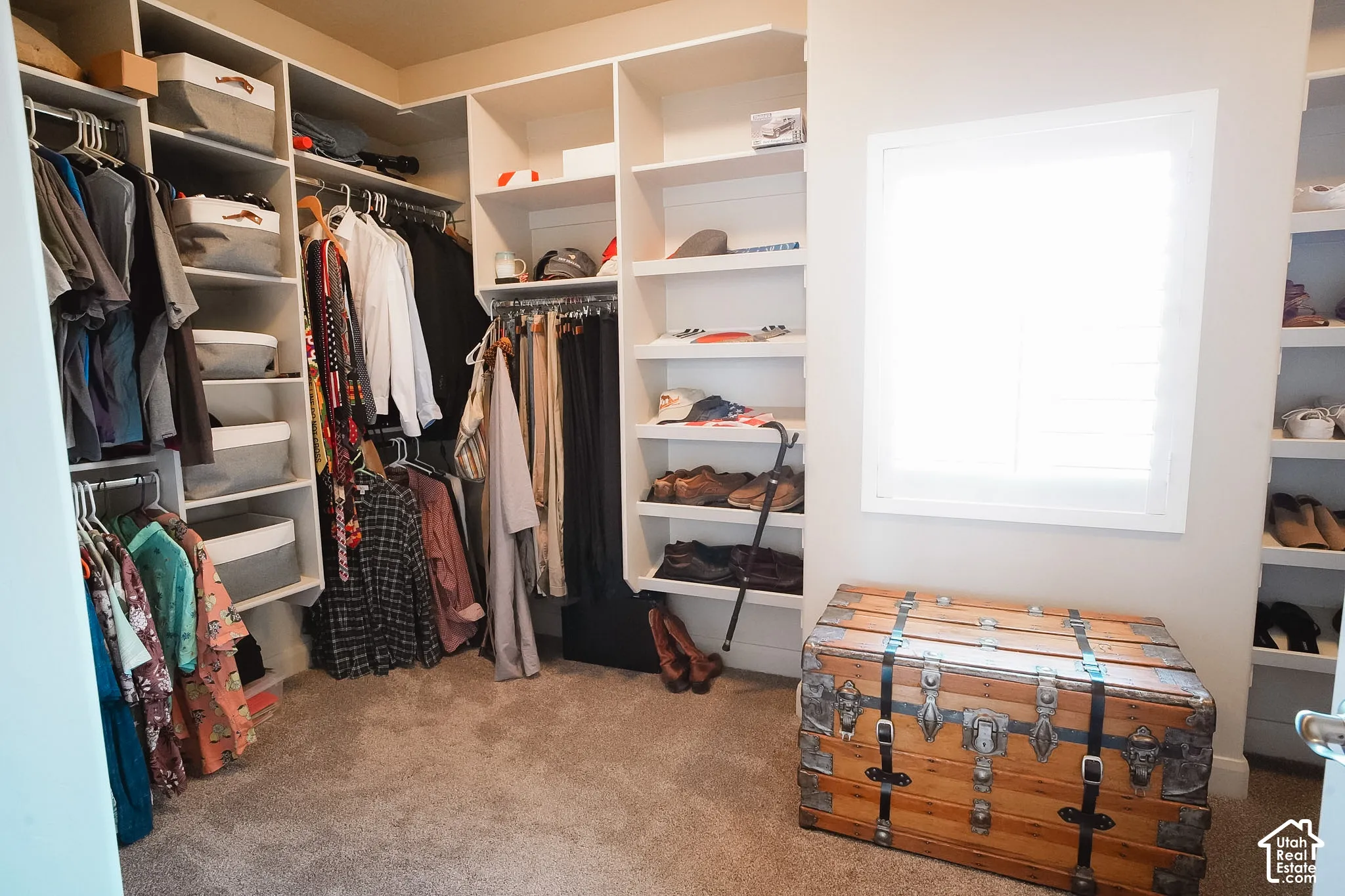 Custom closet system featuring extensive built-in shelving, multiple hanging rods, and an integrated window with white plantation shutters