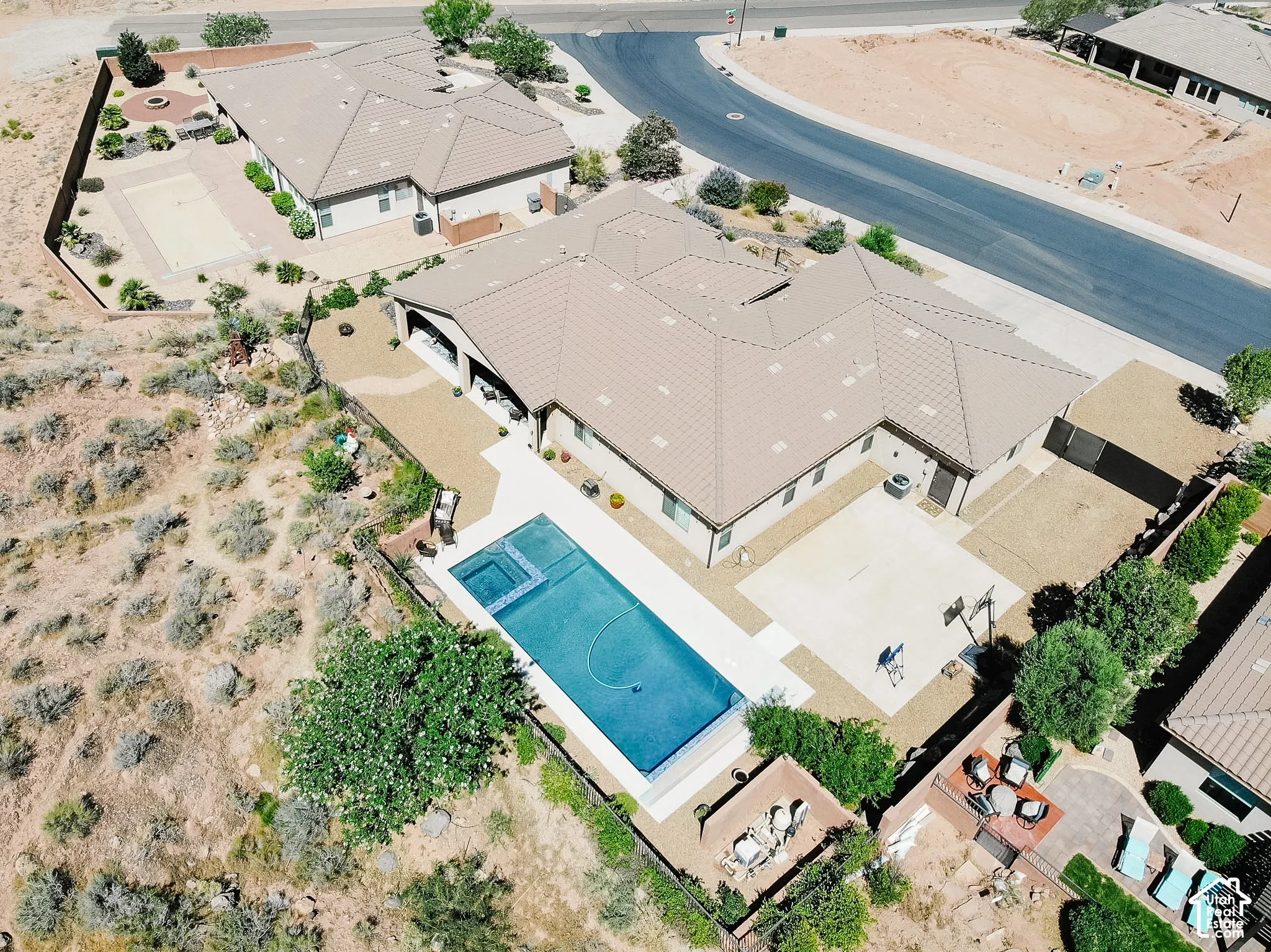 Expansive property featuring a large swimming pool with an integrated spa, extensive hardscaping, and a mature tree line