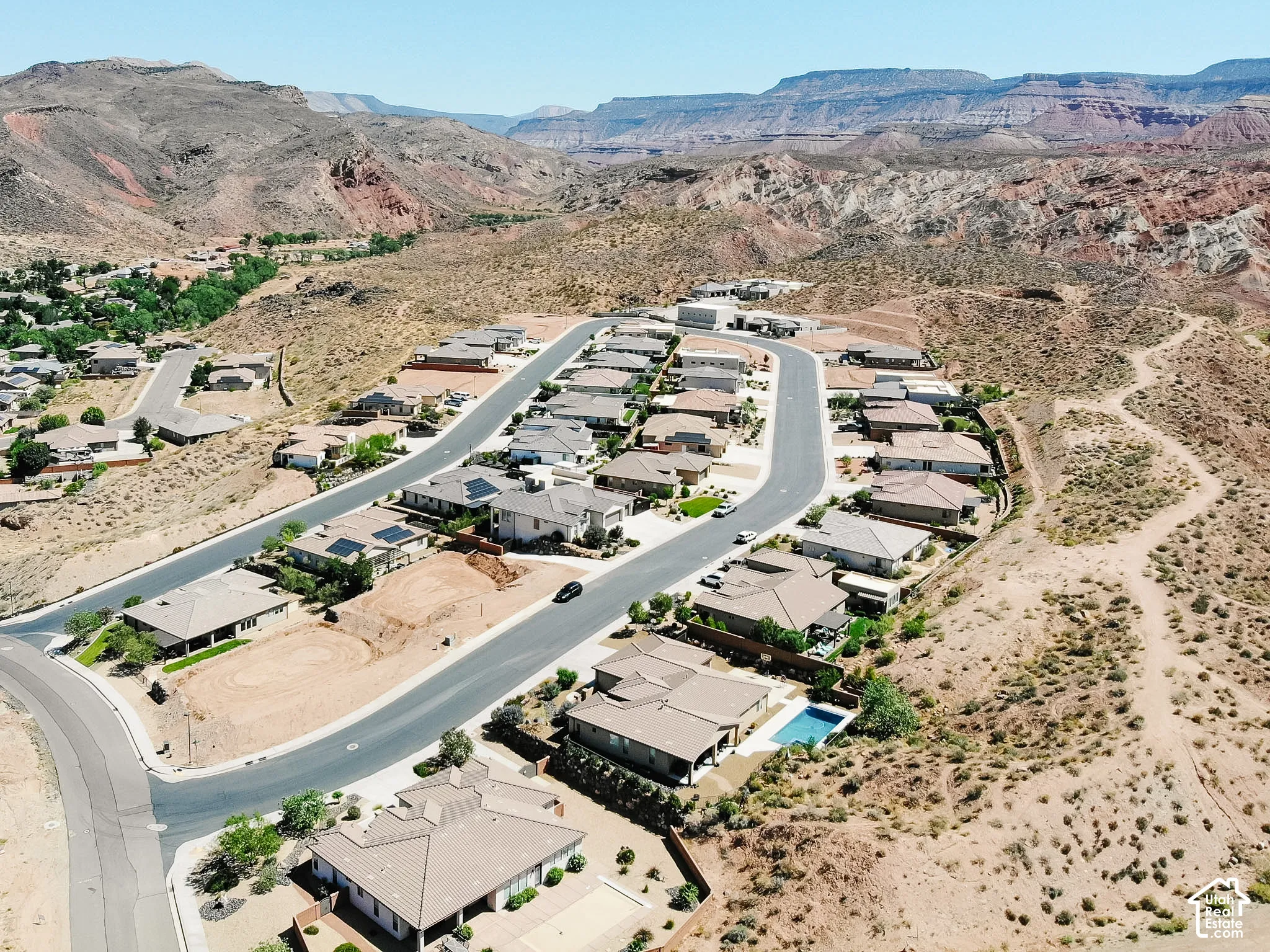 Residential development featuring a winding street, multiple single-story homes with tile roofs, and a backdrop of desert mountains