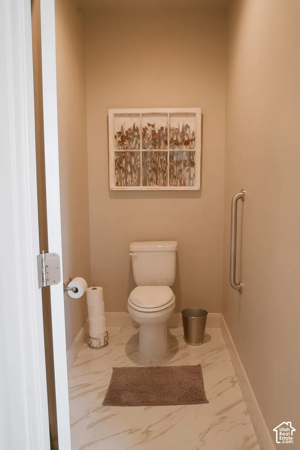Powder room featuring a white toilet, light-toned walls, and marble-look tile flooring