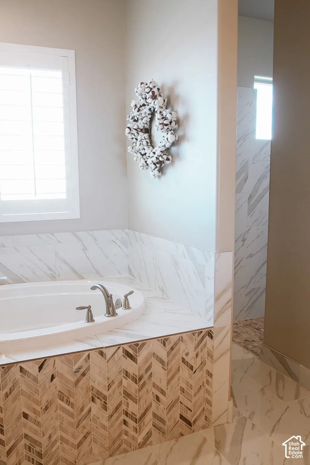 Soaking tub with brushed nickel fixtures, surrounded by marble-look tile
