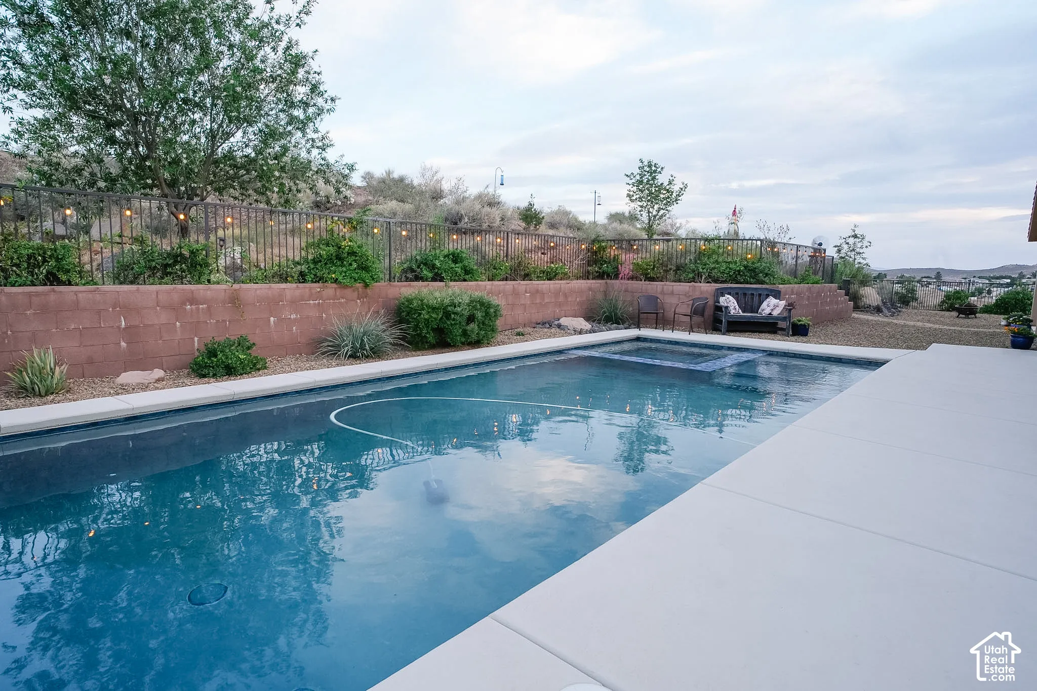 Expansive outdoor living area featuring a rectangular pool with an integrated spa, complemented by a broad concrete patio