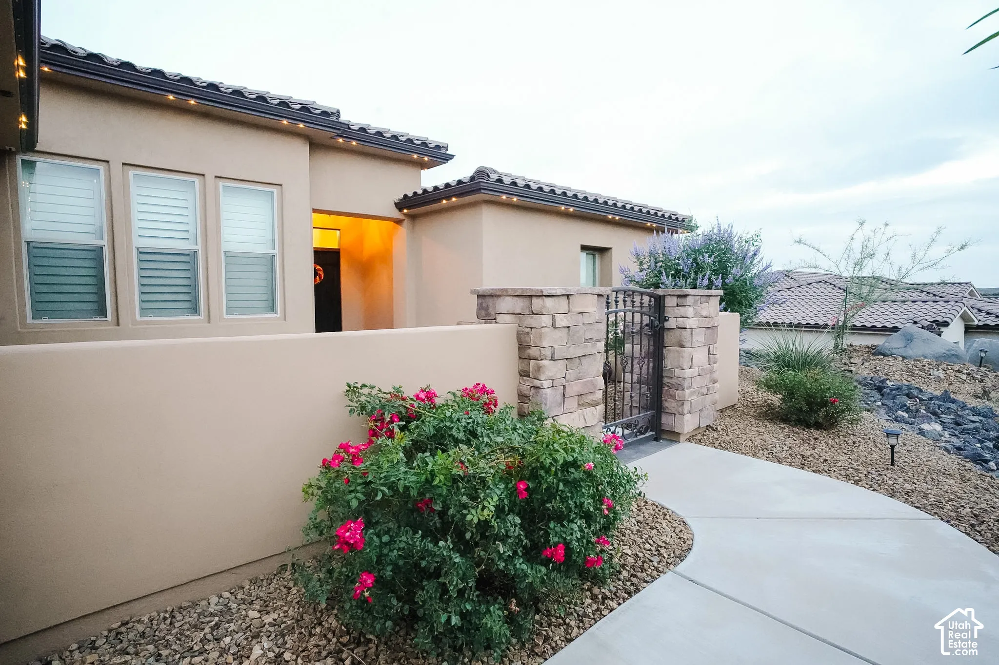 Stucco exterior featuring a stone accent wall, wrought iron gate, and a curved concrete pathway