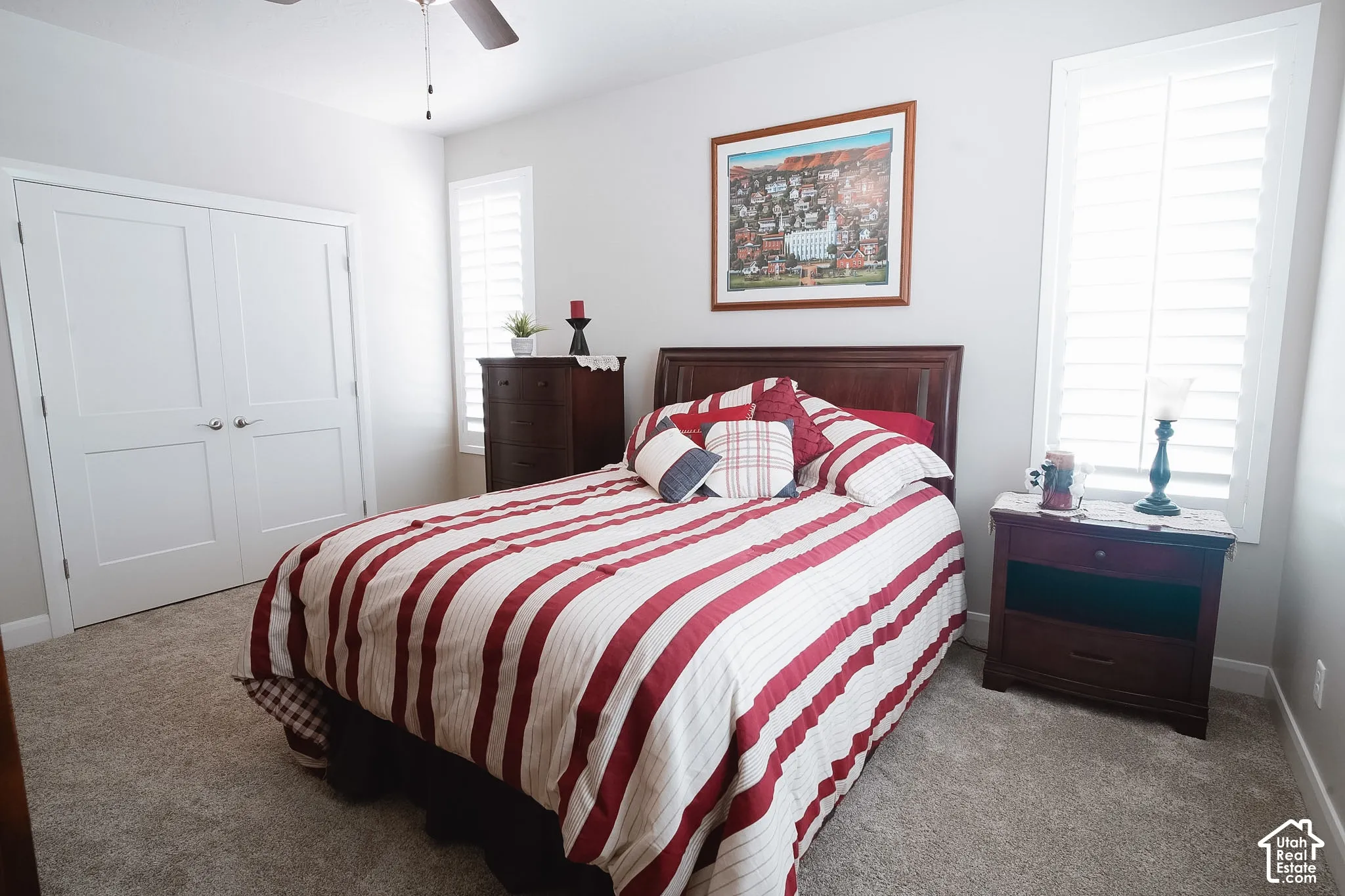 Bedroom featuring light neutral wall paint, plush carpeting, a ceiling fan with integrated lighting, and plantation shutters on multiple windows