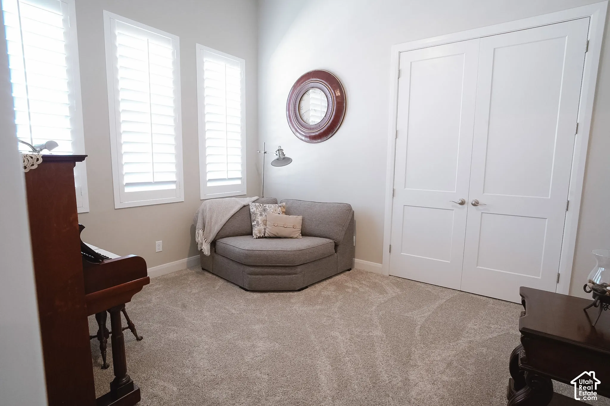 Room featuring white plantation shutters, neutral tone walls, and light-colored carpet flooring