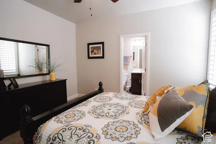 Carpeted room featuring a ceiling fan, window with white plantation shutters, and an entryway to a bathroom with a vanity and toilet