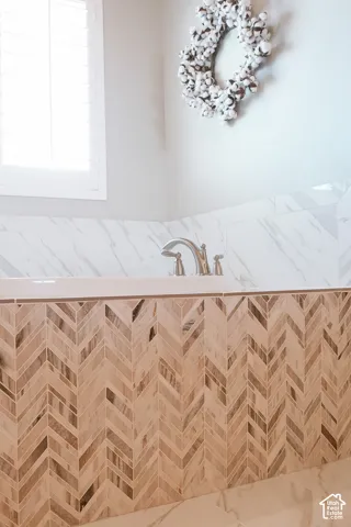 Built-in bathtub featuring a herringbone tile surround, a brushed nickel faucet, and a white marble-patterned tile deck