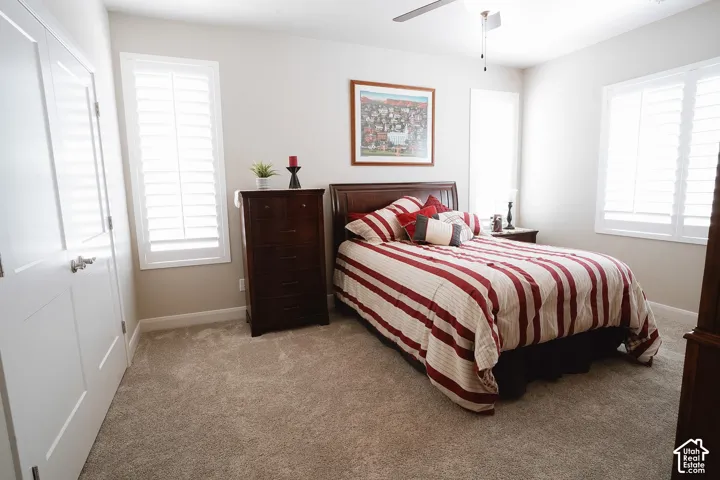 Spacious room featuring carpeting, two windows with white plantation shutters, a ceiling fan, and painted walls