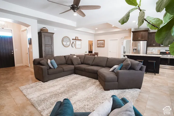 Open-concept living area featuring light-toned tile flooring, tray ceilings, and a ceiling fan with integrated lighting