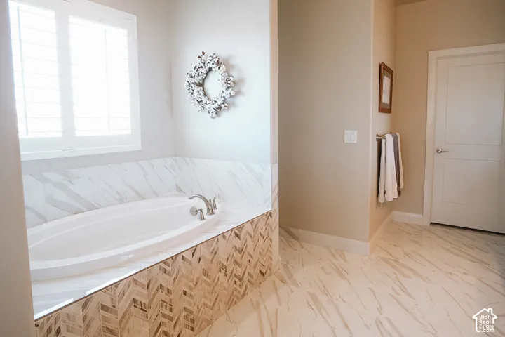 Soaking tub featuring a marble-look surround, decorative herringbone tile accents, and brushed nickel fixtures