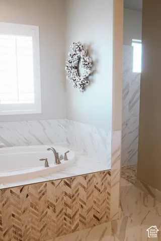 Soaking tub with brushed nickel fixtures, surrounded by marble-look tile