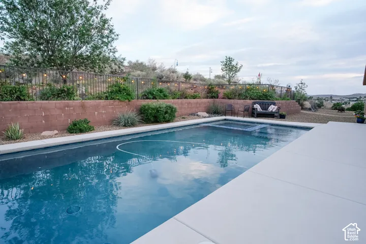 Expansive outdoor living area featuring a rectangular pool with an integrated spa, complemented by a broad concrete patio