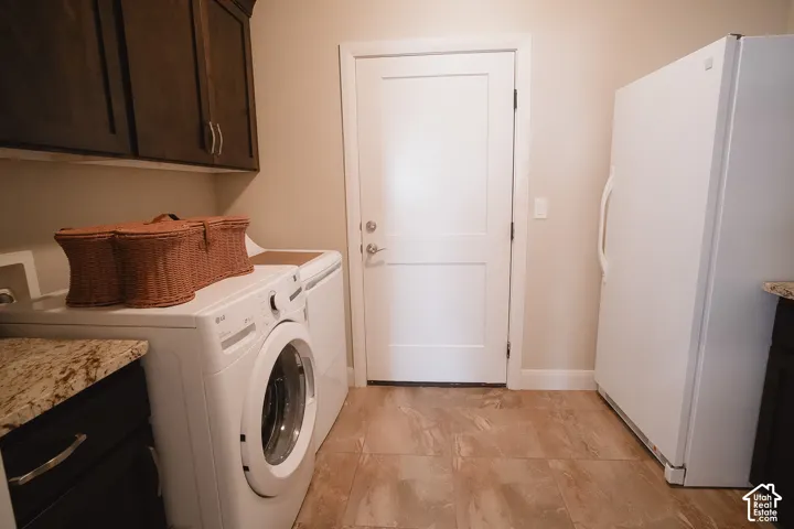 Laundry area featuring dark wood cabinetry, granite-finish countertops, and light-toned tile flooring