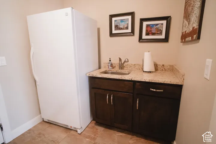 Utility area featuring a built-in base cabinet with a light-colored countertop, an undermount sink with a stainless steel faucet, and tile flooring