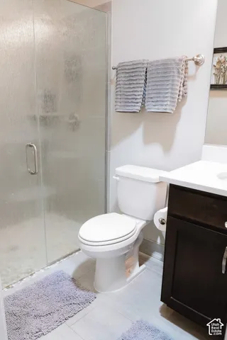 Bathroom featuring a frosted glass shower enclosure, white toilet, dark wood-finish vanity with a white countertop, and light-toned tile flooring