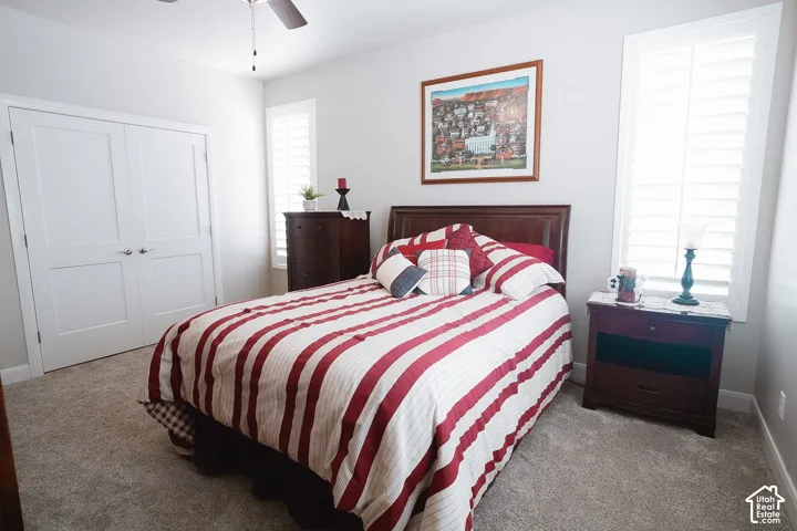 Bedroom featuring light neutral wall paint, plush carpeting, a ceiling fan with integrated lighting, and plantation shutters on multiple windows