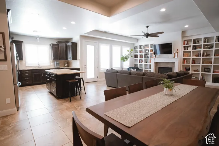 Open-concept living space featuring tile flooring, a kitchen island with seating, dark wood cabinetry, and a living area with extensive built-in shelving and a fireplace