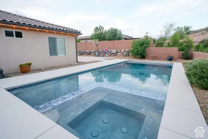 Rectangular swimming pool featuring an integrated spa with jets, surrounded by a light-colored coping