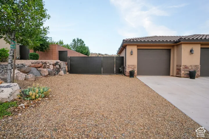 Front exterior featuring a concrete driveway, gravel landscaping, and a dark metal gate