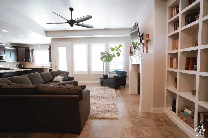 Open-concept living area featuring large format tile flooring, white plantation shutters, a built-in fireplace with mantel, and a wall of built-in shelving