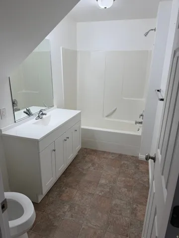 Bathroom with tile flooring, white vanity, integrated sink, and white shower-tub combination