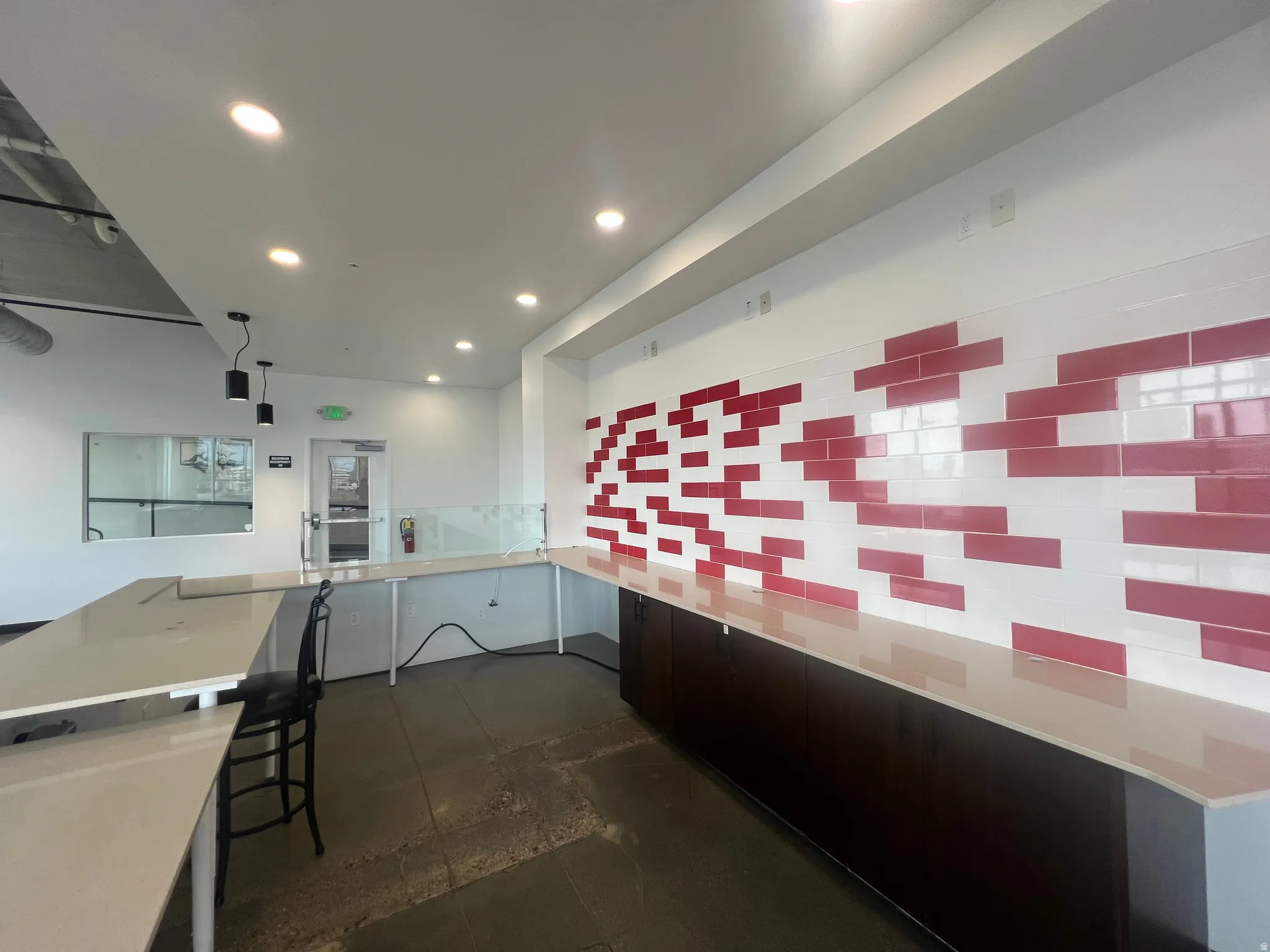 Spacious interior featuring a white and red tiled accent wall, extensive countertop surfaces, dark wood-finish cabinetry, and recessed ceiling lighting