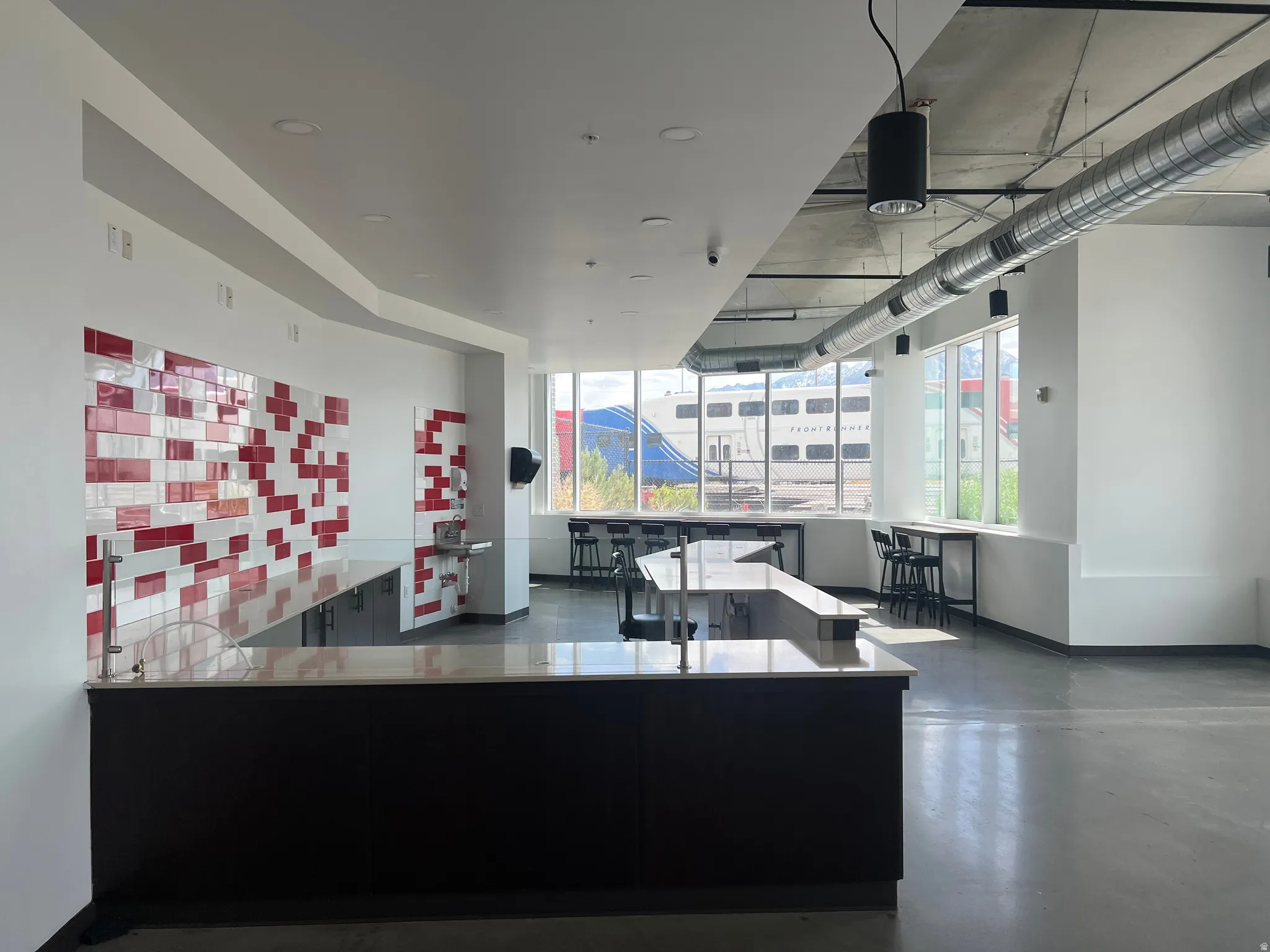 Open-concept space featuring a large central counter with a light-colored surface and dark cabinetry