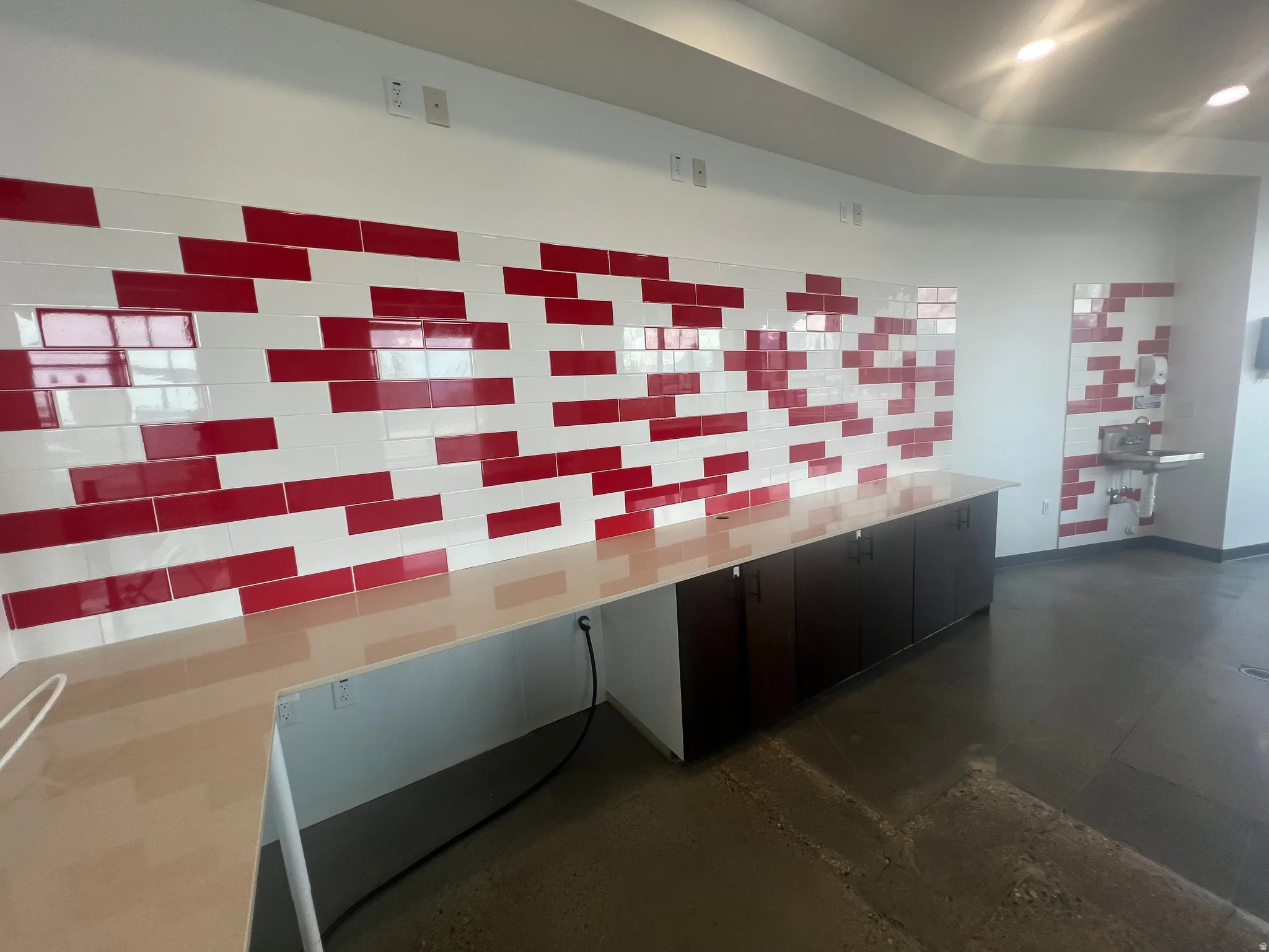 Spacious interior featuring a red and white subway tile accent wall, extensive countertop space, dark wood-finish cabinetry, recessed lighting, and durable concrete flooring