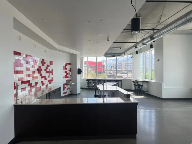 Open concept space featuring a large central island with a light-toned countertop, extensive windowline, exposed ductwork, concrete flooring, and a red and white tiled accent wall