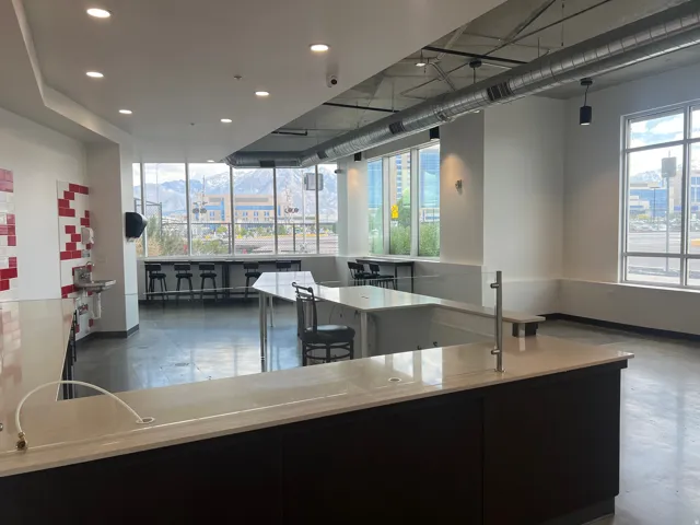 Spacious open-concept commercial interior featuring floor-to-ceiling windows, exposed industrial ductwork, polished concrete flooring, a large service counter with a light-toned countertop, and modern recessed lighting